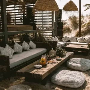 Strefa odpoczynku bądź restauracja w okolicach plaży z naturalnymi meblami oraz słomkowymi lampionami. Na stole podane są przekąski.