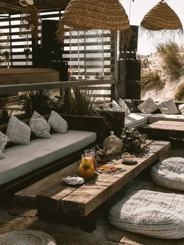 Strefa odpoczynku bądź restauracja w okolicach plaży z naturalnymi meblami oraz słomkowymi lampionami. Na stole podane są przekąski.